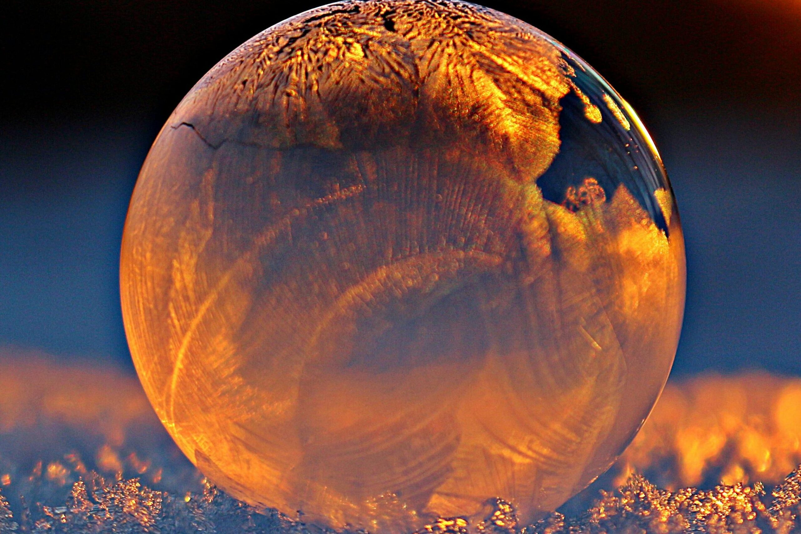 Close-up shot of a frozen bubble with warm reflections resting on a snowy surface at twilight.